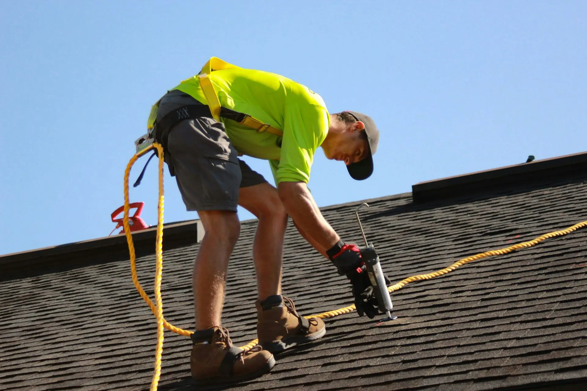 Roofer sealing shingles with a caulk gun during a roof leak repair