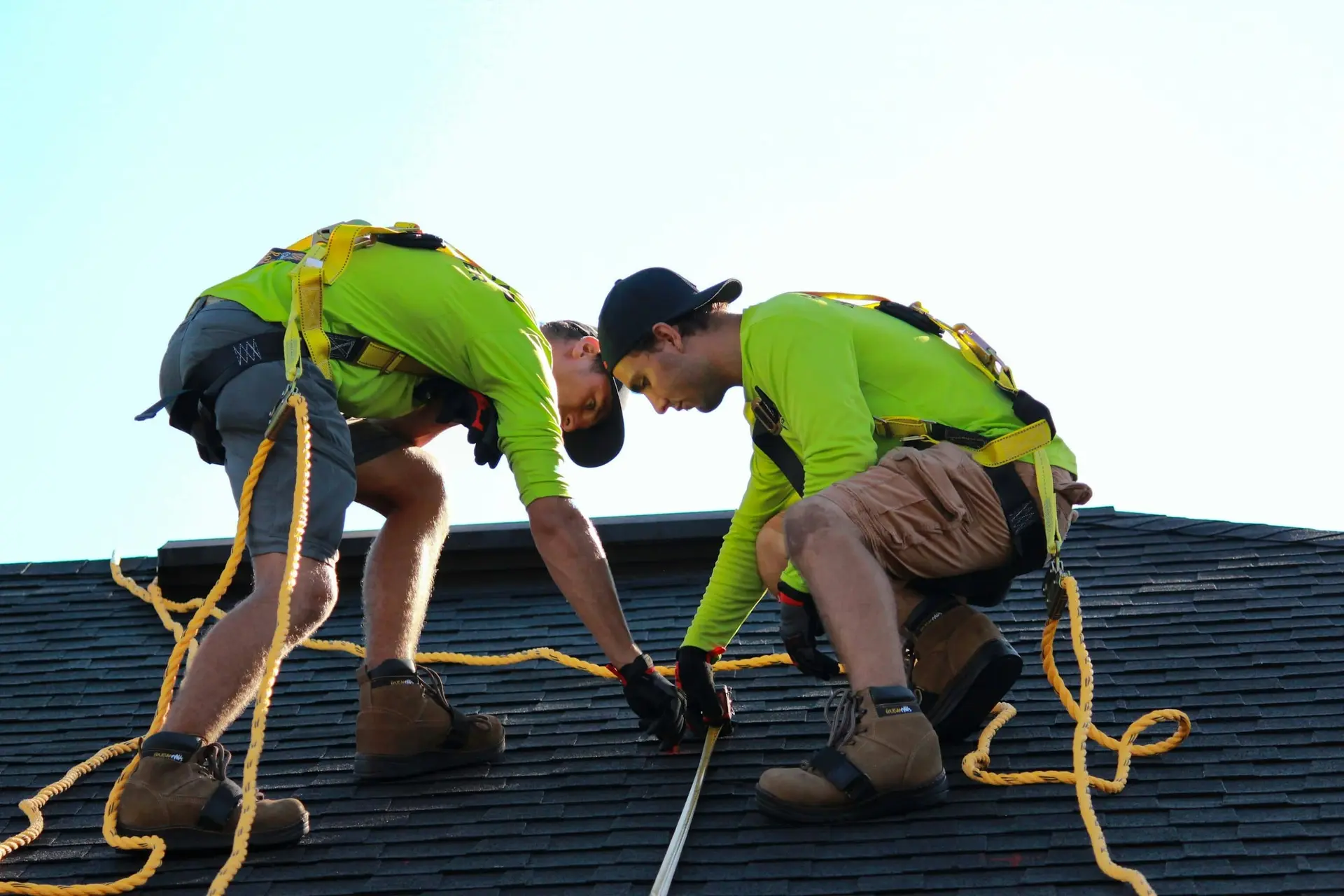 Two roofers tied off with safety lines working on a shingle roof
