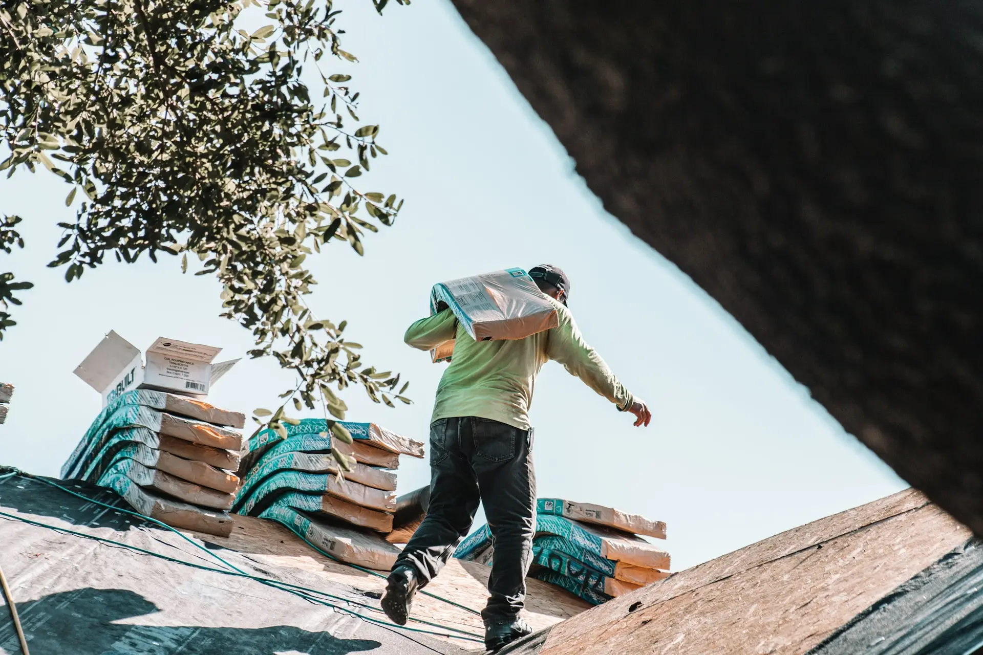 Roofer carrying bundles of shingles across a residential roof